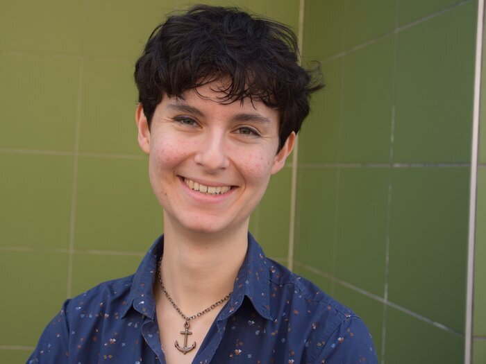 Foto von Clara: Eine Person mit kurzen Haaren und blauem Hemd lächelt in die Kamera